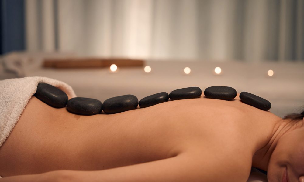 Cropped photo of naked lady lying prone with smooth flat hot stones placed along her spine