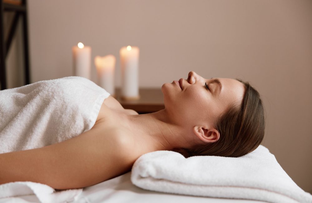 Side view of peaceful woman with closed eyes and covered towel relaxing after massage session at spa salon. Rest and stress relief at wellness center